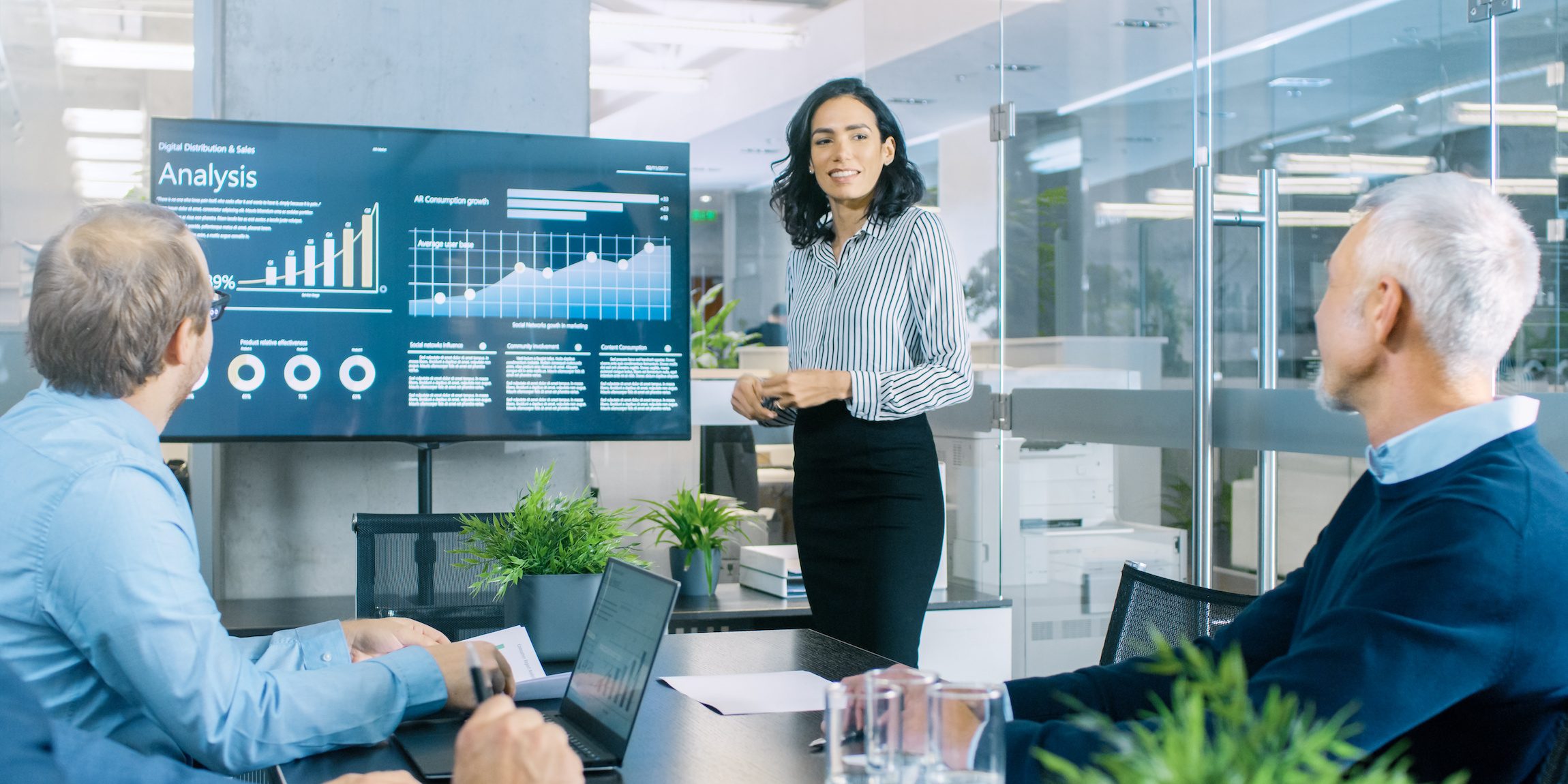 Chief Female Executive Gives a Report/ Presentation to Her Colleagues in the Meeting Room, She Shows Graphics, Pie Charts and Company’s Growth on the Wall TV. Building a Top-Tier Executive Consumer Goods Sales Team: A Guide by Hunter & Michaels