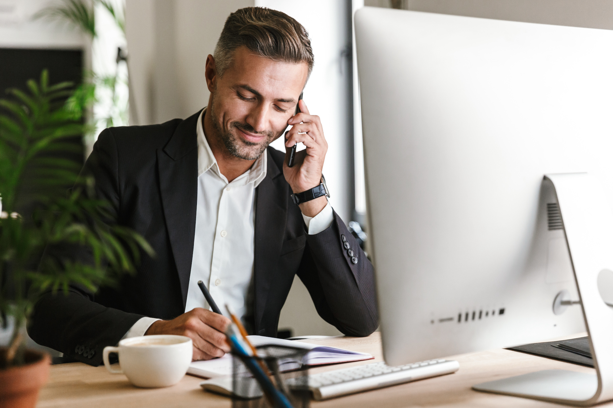 Image of handsome businessman talking on cell phone while working on computer in office When It's Time to Work with a CPG Agency: Insights from Hunter & Michaels