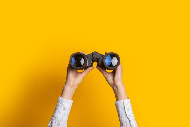 female hands hold black binoculars on a bright yellow background Common Pitfalls in Consumer Brand Hiring and How to Avoid Them