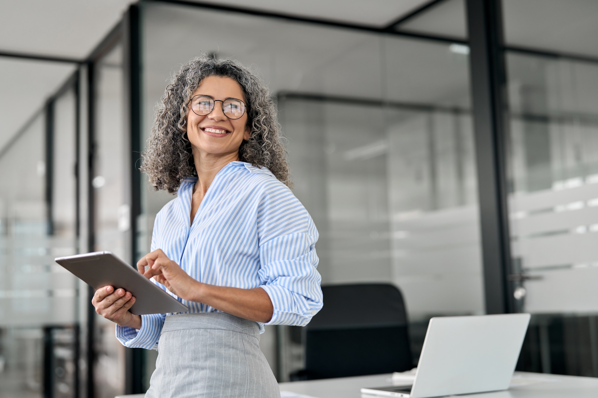 Smiling mature professional business woman holding tab looking away in office. Partnering with Hunter & Michaels, a Leading CPG Agency, for Your Staffing Needs